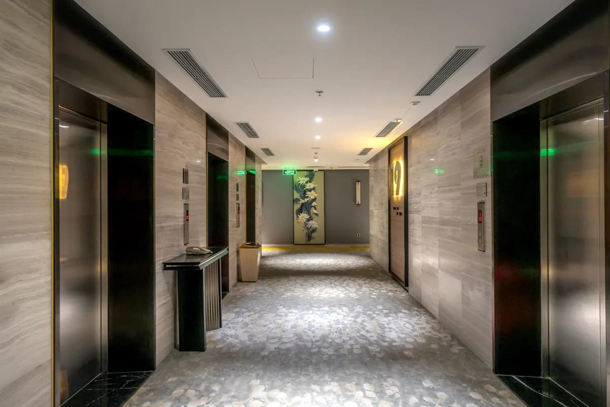 Imagen de ejemplo de BookNoFees: pasillo de hotel con elevadores y alfombra gris