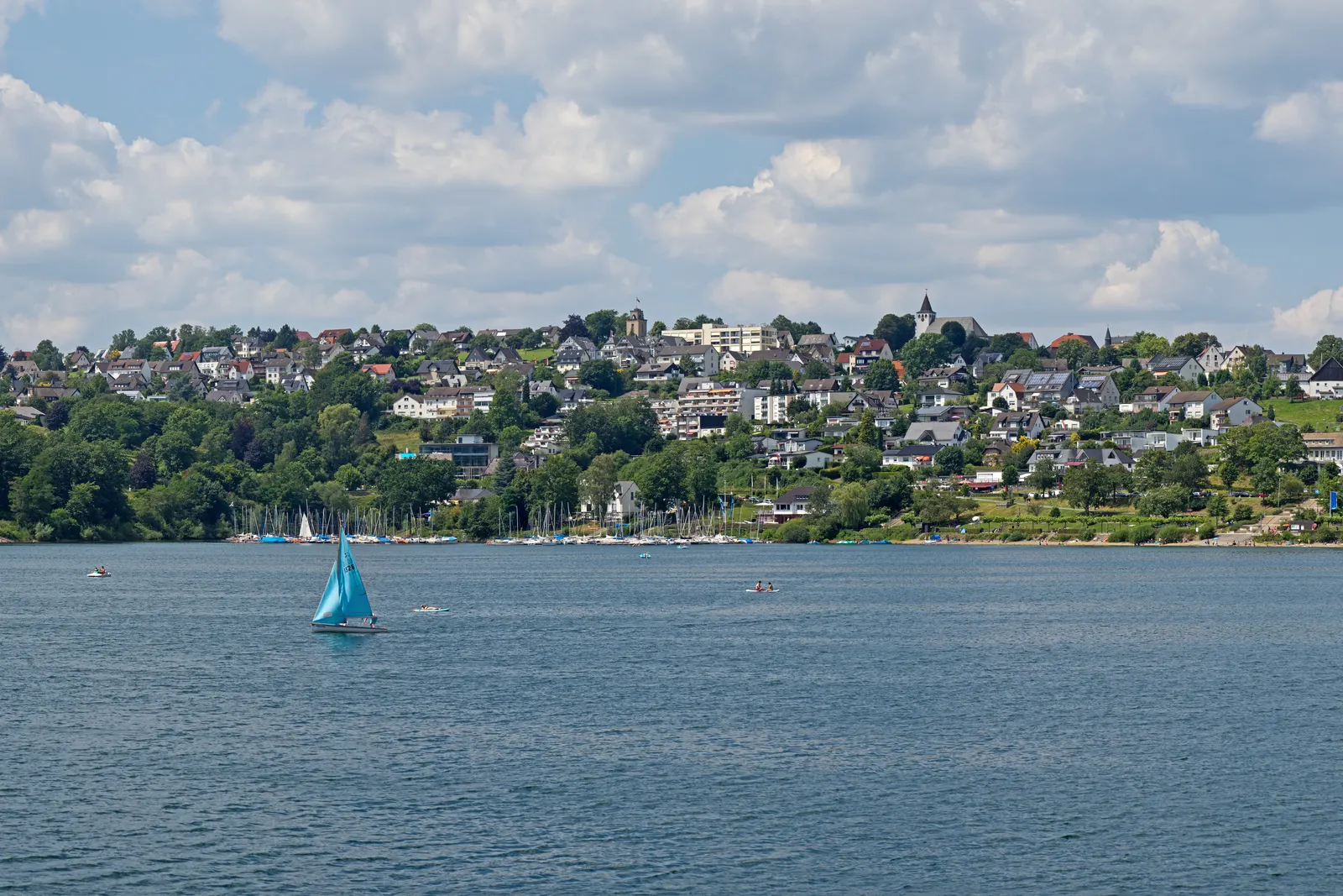 Langscheid, a orillas del lago Sorpesee, cerca de Sundern: el pueblo a orillas del lago, elevado sobre el agua, con un velero al frente