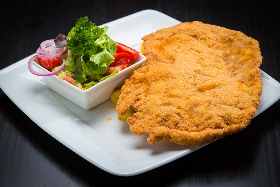 BookNoFees: Foto de ejemplo: Schnitzel empanizado con una ensalada de acompañamiento en un plato blanco