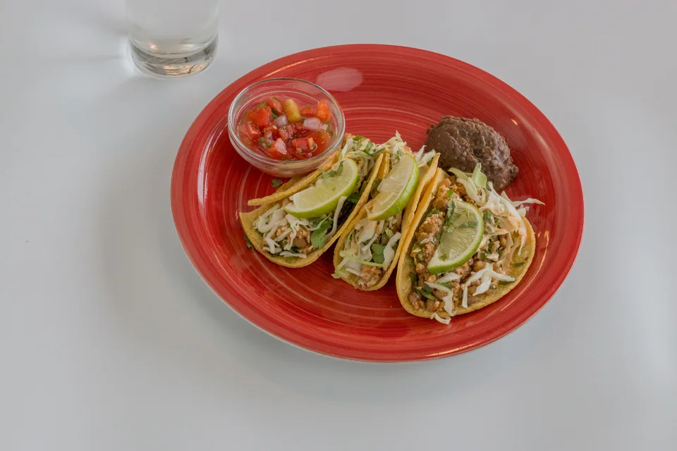 BookNoFees: Foto de ejemplo: Tres tacos adornados con rodajas de lima y salsa, servidos en un plato rojo