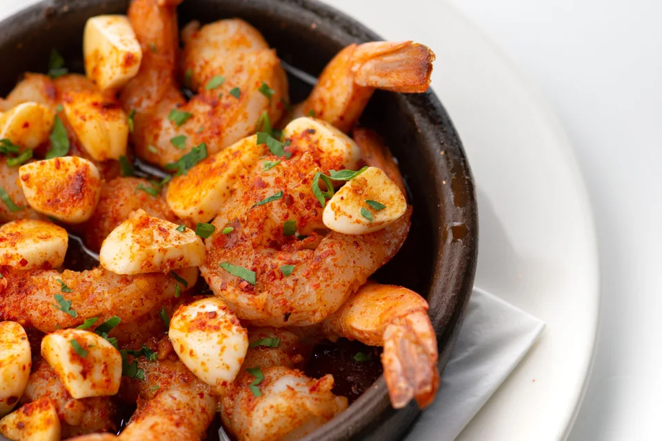 Foto de ejemplo: Camarones al ajillo adornados con hierbas picadas en un tazón negro sobre un plato blanco