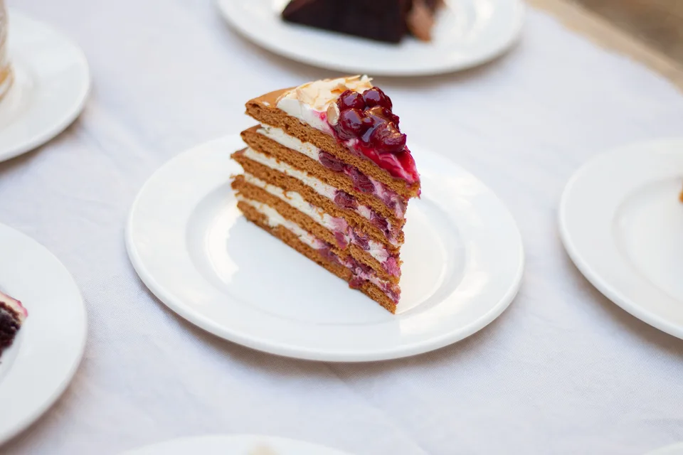 Foto de ejemplo: Una rebanada de pastel de capas decorada con frutos rojos en un plato blanco