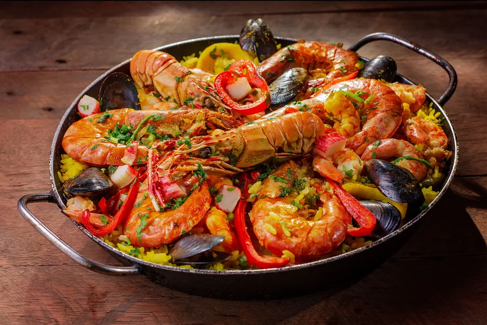 BookNoFees: Foto de ejemplo: Una cacerola de paella de mariscos con conchas y pimientos rojos por encima